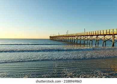 Fishing Pier On The Atlantic Ocean, Sunset Beach, North Carolina At Sunrise With A Clear Blue Sky