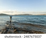 Fishing for pike, perch, carp. Fisherman with rod, spinning reel on sea or ocean. Man catching fish, pulling rod while fishing on sea, pond. Wild nature. The concept of rural getaway. Back view.