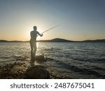 Fishing for pike, perch, carp. Fisherman with rod, spinning reel on sea or ocean. Man catching fish, pulling rod while fishing on sea, pond. Wild nature. The concept of rural getaway. Back view.
