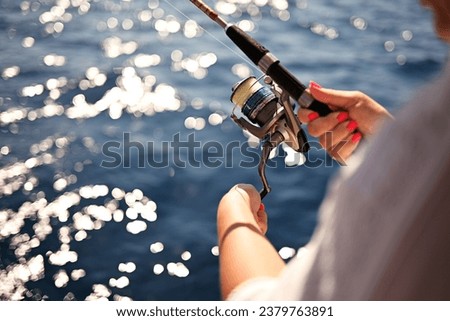 A fishing rod with fishing line in the hands of a fisherman standing on the deck of a boat in the sea. Sea waves and sun reflection in water