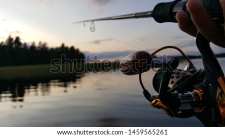 Fishing rod wheel closeup, beautiful lake and trees reflections in the lake