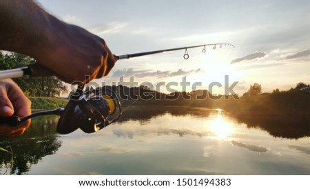 Fishing rod wheel closeup, man fishing on a lake with a beautiful sunrise/sunset behind him