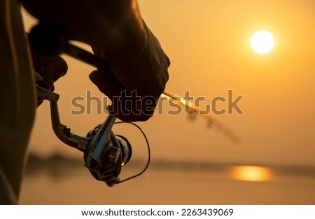Fishing rod wheel closeup, man fishing in lake with a beautiful sunrise.