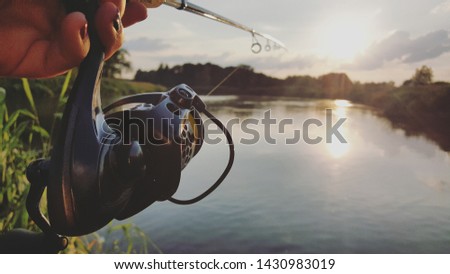 Fishing rod wheel closeup, woman fishing with a beautiful sunrise/sunset behind her