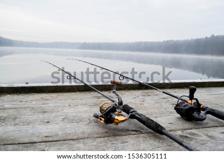 Fishing rod and wheels on the wooden pier, misty fog against the backdrop of lake. The concept of rural getaway. Article about fishing day.