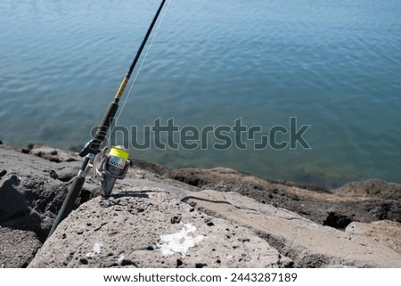 Fishing rod with yellow fishing line clamped in a crevice between rocks of a seaside quay