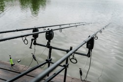 Fishing Rods For Carp Fishing With Signaling Devices On Holder. Rod Pod. Fishing For Pike, Perch, Carp On Background Of Lake And Nature.  Misty Morning. Wilderness Area. Fishing In Rainy Weather, Rain