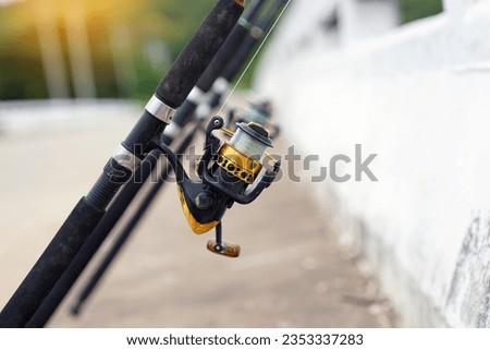 Fishing rods lay across the edge of the bridge in rows waiting for the fish to eat their prey. Focus on a spinning reel that can release the fishing line well over long distances.                     