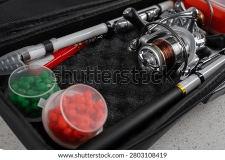 Fishing tackle set containing a compact rod, spinning reel with line, and small containers of artificial bait inside an open black padded case.