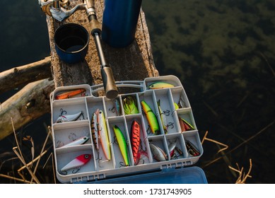Fishing Tackle - Fishing Spinning, Rod, Reel, Hooks, Fly, Bait, Lures In Box On Wooden Pier On Pond Background. Fishing Day. Top View. Fishing For Pike, Perch. Recreation. Vintage Banner. Closeup.