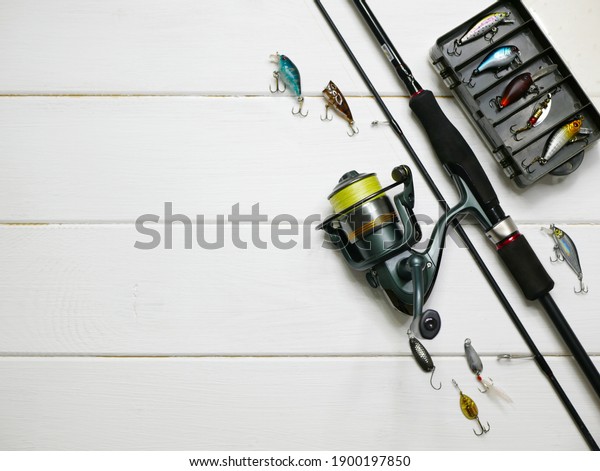 Fishing tackles lay on white wooden boards. Set of\
fishing tackles. Top view on spool, rod, spoons, wobblers and lure\
box.