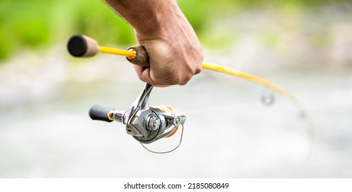 Fishings reel close-up on the background of the river. Fisherman hand holding fishing rod with reel. Fishing Reel. Fishing Rod with Aluminum Body Spool.