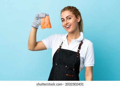 Fishmonger wearing an apron and holding a raw fish over isolated blue background