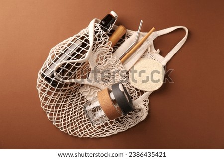 Fishnet bag with different items on brown background, top view. Conscious consumption