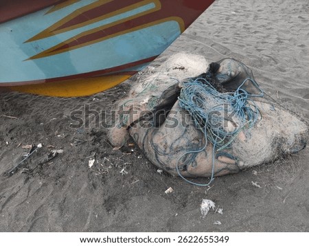 Fishnet and rope below a fisherman harbored fiber boat after fishing in the sea at the sandy beach. 
