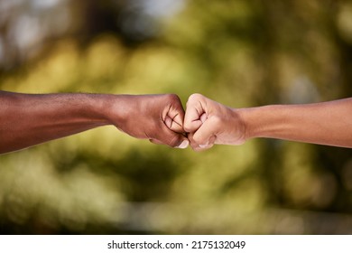 Fist Bump Of Two Interracial Men Outdoor Against A Blur Background. Closeup Of Diverse Athletes Doing Social Gesture Greeting In A Park. Showing Solidarity, Friendship, Brotherhood, Teamwork Or Unity