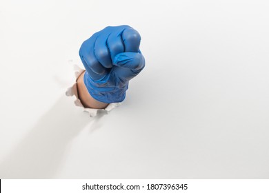 Fist In A Latex Glove Kicking Through Torn White Wall With Copy Space. Stay Strong, Healthy And Kick COVID-19 Out.