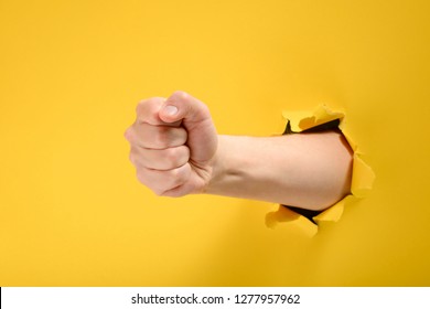 Fist punching through yellow paper background. Threat, fight and combat sports. Push through the wall.
