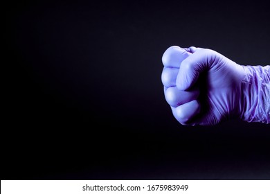 Fist Of Right Man Hand In A Purple Medical Glove On A Black Background