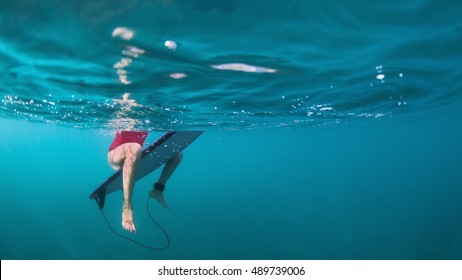 Fit active girl in bikini. Surfer on surf board wait for ocean wave. Woman feet and surfboard underwater photo. People in water sport adventure camp. Swimming, extreme surfing on summer beach holiday

