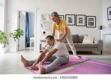 Fit active retired middle aged wife helping senior husband doing stretching exercise at home. Happy healthy older senior 60s couple enjoying fitness sport training workout together in apartment. - Powered by Shutterstock