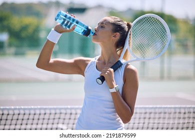 Fit and active tennis player drinking water from a bottle after practicing, training and playing on a sports court or club. Thirsty professional sportswoman hydrating while holding a racket outside - Powered by Shutterstock