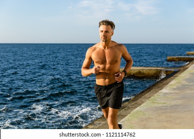 fit adult shirtless man jogging on seashore - Powered by Shutterstock