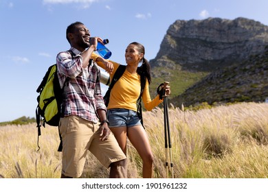 Fit Afrcan American Couple Wearing Backpacks Nordic Walking With Poles Drinking Water In Mountain Countryside. Healthy Lifestyle, Exercising In Nature.