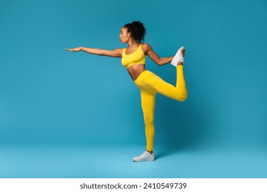 Fit African American Lady Stretching Raised Leg And Extending Arm, Practicing Balance Exercise On Blue Background. Full Length Of Woman Exercising In Lord Of The Dance Pose Doing Yoga In Studio - Powered by Shutterstock