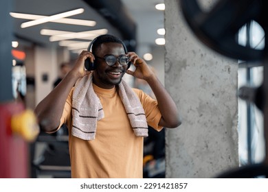 Fit African American man listening to music in gym, adjusting headphones, feeling satisfied and happy, smiling while enjoying the rhythm of music song during exercising workout routine. - Powered by Shutterstock