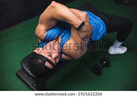 A fit asian guy suffers from a torn or hyperextended tricep on a bench while working out. Common arm workout injury.