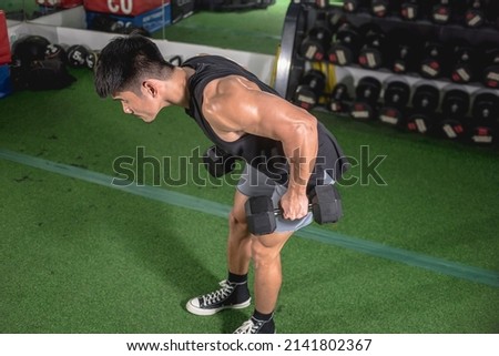 A fit asian man does bent-over dumbbell rows. Weight and resistance training at the gym.