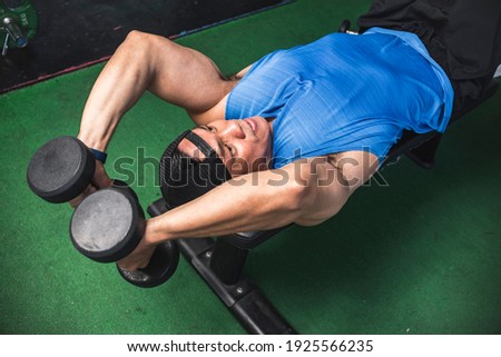 A fit asian man does a set of lying dumbbell tricep extensions. Working out Triceps and arms at the gym.