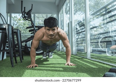 A fit asian man does some regular push-ups near the window of an upscale gym. Warming up or doing body weight exercises. - Powered by Shutterstock