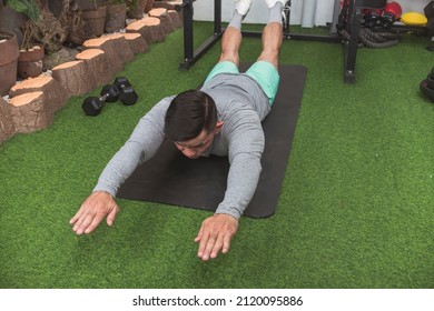 A fit asian man does Superman Back Extensions on a black mat. Isometric exercise. Working out and training lower back muscles at a home gym.