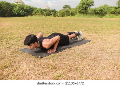 A fit asian man doing regular pushups at an open field outdoors. Torso lowered until chest is almost touching the mat.