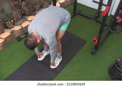 A Fit Asian Man In A Gray Sweater Does Standing Toe Touch Stretches. Warming Up Before A Workout At His Home Gym.