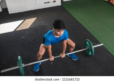 A fit asian man prepares to do a set of barbell sumo deadlifts. Using an overhand grip. About to lift weights from the floor. Working out at the gym. Overhead shot.