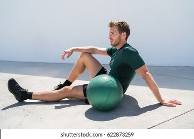 Fit Athlete Man Relaxing At Fitness Gym During Medicine Ball Workout. Healthy And Active Lifestyle Young Adult Portrait.