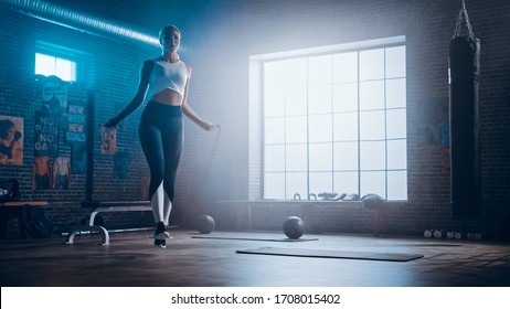 Fit Athletic Blond Woman Exercises With Jumping Rope In A Loft Style Industrial Gym. She's Concentrated On Her Intense Fitness Training Program. Facility Has Motivational Posters On The Wall.