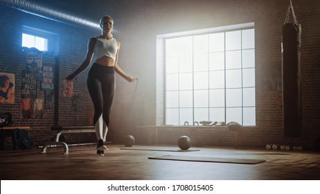 Fit Athletic Blond Woman Exercises With Jumping Rope In A Loft Style Industrial Gym. She's Concentrated On Her Intense Cross Fitness Training Program. Facility Has Motivational Posters On The Wall.