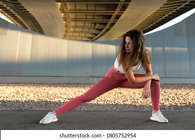 Fit athletic woman doing workout before jogging under the bridge. Young fitness female runner stretching legs while warming up under the bridge outdoors  - Powered by Shutterstock