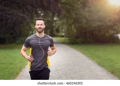 Fit bearded young man jogging through a park listening to music on his mobile phone, upper body approaching the camera with copy space - Shutterstock ID 460196392