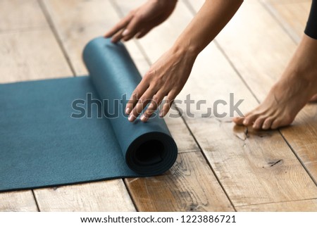 Fit beautiful woman folding blue exercise mat on wooden floor before or after working out in yoga studio club or at home Top close up view. Equipment for fitness, pilates or yoga, well being concept