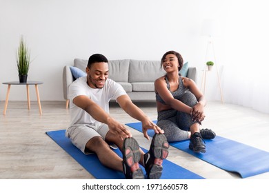 Fit black couple exercising on yoga mats at home, full length. Happy African American guy doing flexibility workout, his girlfriend taking break from training. Healthy lifestyle during covid-19 - Powered by Shutterstock