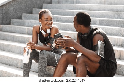 Fit Black Couple Taking Rest After Workout Outdoors, Sitting On Urban Stairs, Drinking Water And Coffee And Chatting, Free Space - Powered by Shutterstock