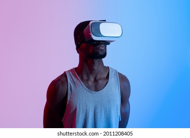 Fit Black Guy Wearing VR Headset, Exercising With Virtual Reality Gear In Neon Lighting. Young African American Man Using Modern Technologies For Online Workout, Enjoying Sports Simulation