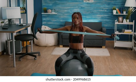 Fit Black Woman Doing Yoga Exercices Using Elastic Bands On Swiss Ball In Living Room Practicing Sport. Atheltic Lifting Training Healthy Lifestyle Sport Fitness Workout At Home With Weights Dumbbell