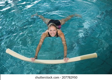 Fit blonde swimming with foam roller in swimming pool at the leisure centre