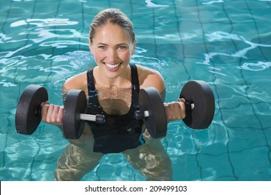Fit blonde working out with foam dumbbells in swimming pool at the leisure centre
